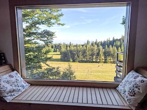 A window seat with a view of a grassy field and trees.