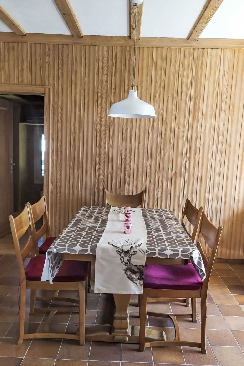 Un coin repas avec une table en bois, quatre chaises, une nappe à motifs et un luminaire suspendu.