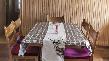 Un coin repas avec une table en bois, quatre chaises, une nappe à motifs et un luminaire suspendu.