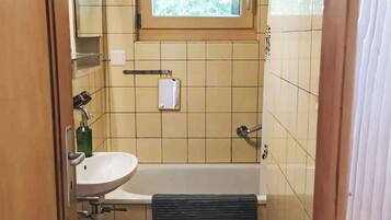 Une salle de bain avec une fenêtre, un lavabo, une baignoire et un porte-serviettes.