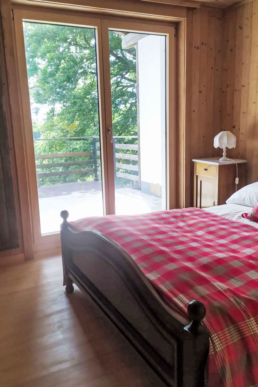 Une chambre à coucher comprenant un lit, une table de chevet, une lampe et une porte coulissante donnant sur un balcon extérieur.