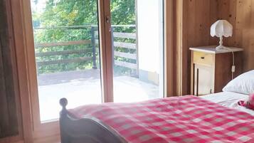 Une chambre à coucher comprenant un lit, une table de chevet, une lampe et une porte coulissante donnant sur un balcon extérieur.