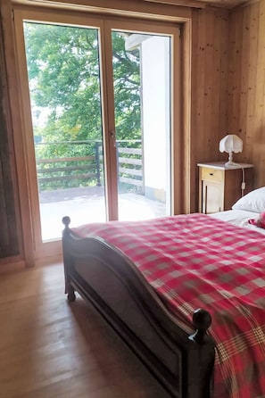 A bedroom with a bed, a nightstand, a lamp, and a view through a sliding door to an outdoor balcony.