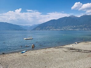 A lake with boats, a pebble beach, and mountains in the background. - Apt. Blu Celeste by Interhome (Magadino)