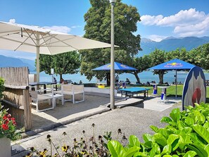 An outdoor seating area with tables and chairs, a pool table, and umbrellas. - Apt. Blu Celeste by Interhome (Magadino)