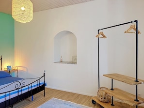 A bedroom with a bed, a hanging light fixture, a mirror, and a clothing rack. - Apt. Blu Celeste by Interhome (Magadino)