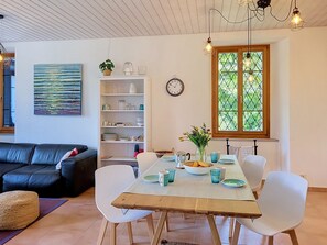 A dining area with a wooden table, white chairs, and a window with a view of greenery. - Apt. Blu Celeste by Interhome (Magadino)