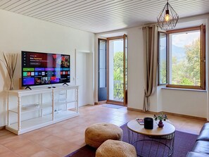 A modern living room with a flat-screen TV, a white console table, a round coffee table, and a view of the outdoors through a glass door. - Apt. Blu Celeste by Interhome (Magadino)