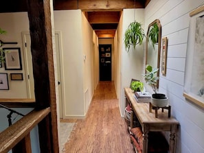 A narrow hallway with wooden flooring, a wooden bench with plants, and a mirror on the wall. - Unique and Spacious Home in Quiet NW Bend - King & Queen Beds - Large Yard (Bend)