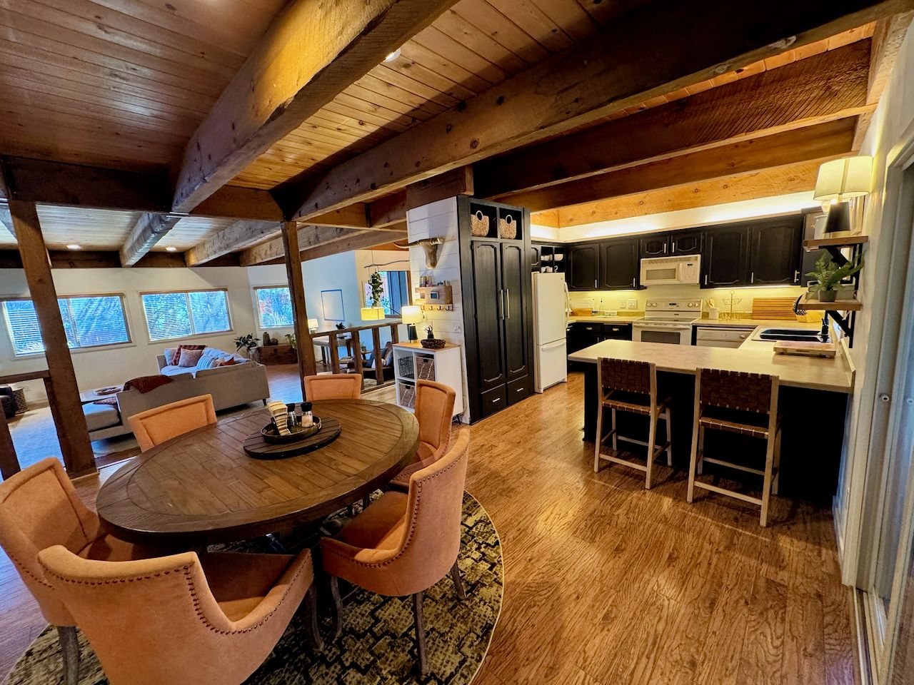 Eine moderne Küche mit Holzbalken, ein Essbereich mit rundem Tisch und Stühlen sowie ein Blick zum Wohnzimmer.