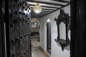 Un corridoio interno con porte nere decorate, un lampadario e un grande specchio a parete.