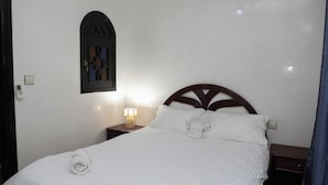 Uma cama bem arrumada com cabeceira de madeira, luminária de mesa e interruptor de luz na parede.