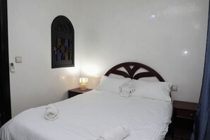 A neatly made bed with a wooden headboard, a bedside lamp, and a wall-mounted light switch. - The Riad Kenyandha - Fiber Optics · Swimming Pool · Italian Oven (Marrakech)