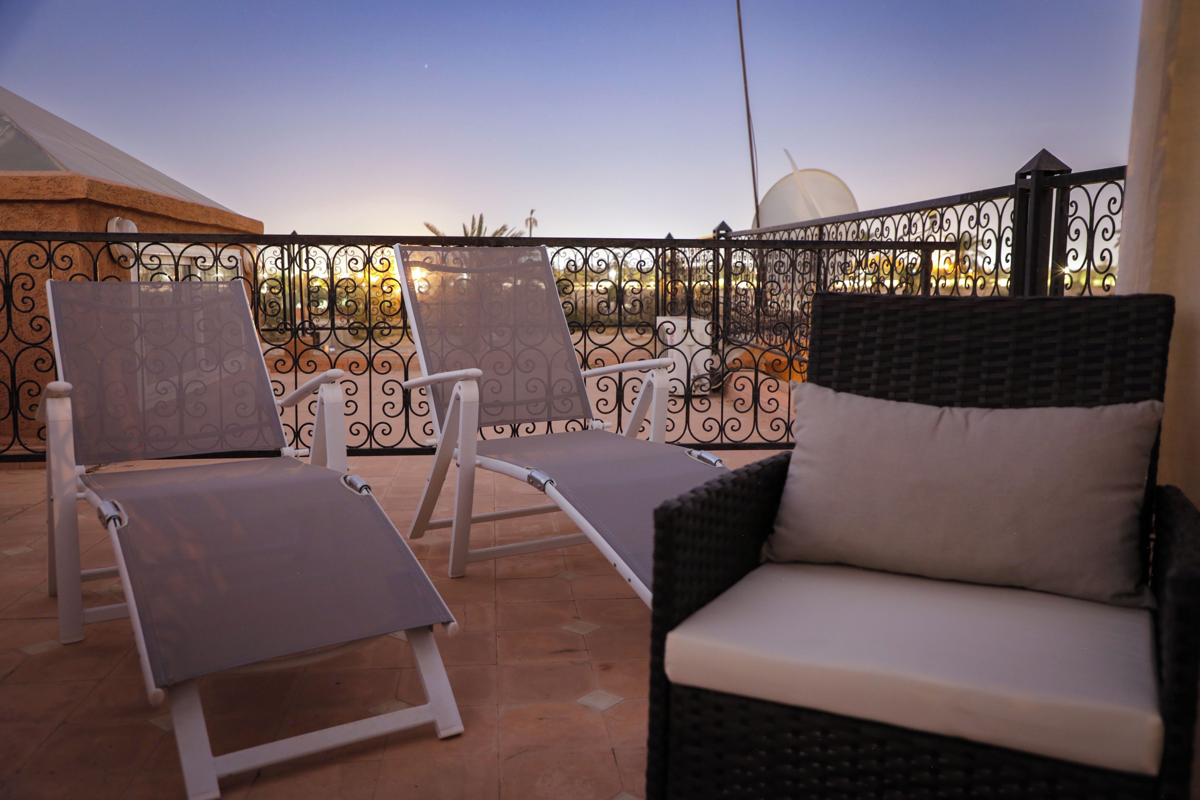 A terrace with two lounge chairs and a sofa, surrounded by a decorative metal fence.