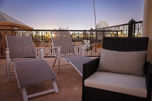 Eine Terrasse mit zwei Liegestühlen und einer Couch, umgeben von einem schmiedeeisernen Geländer.