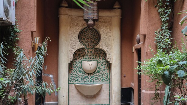 Um pátio tradicional marroquino com uma fonte, paredes azulejadas e plantas em vasos.