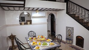 Uma área de refeições com mesa posta para o café da manhã, rodeada por cadeiras, e uma escada com corrimãos decorados.