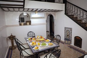 A dining area with a table set for breakfast, surrounded by chairs, and a staircase with ornate railings. - The Riad Kenyandha - Fiber Optics · Swimming Pool · Italian Oven (Marrakech)