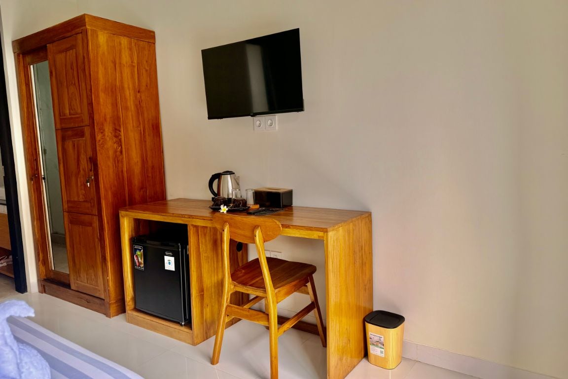 A room with a wooden desk, a chair, a television mounted on the wall, and a small refrigerator.