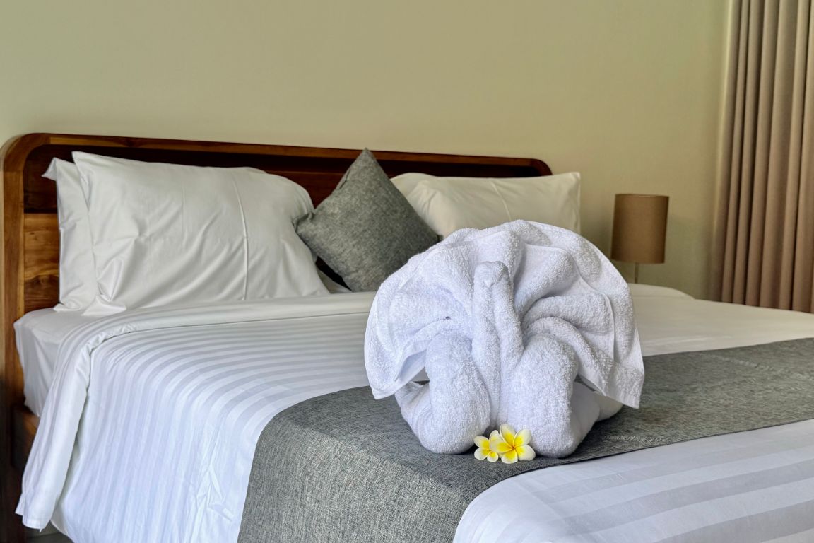 Una cama bien hecha con sábanas blancas, una almohada gris y una toalla con un estampado floral.