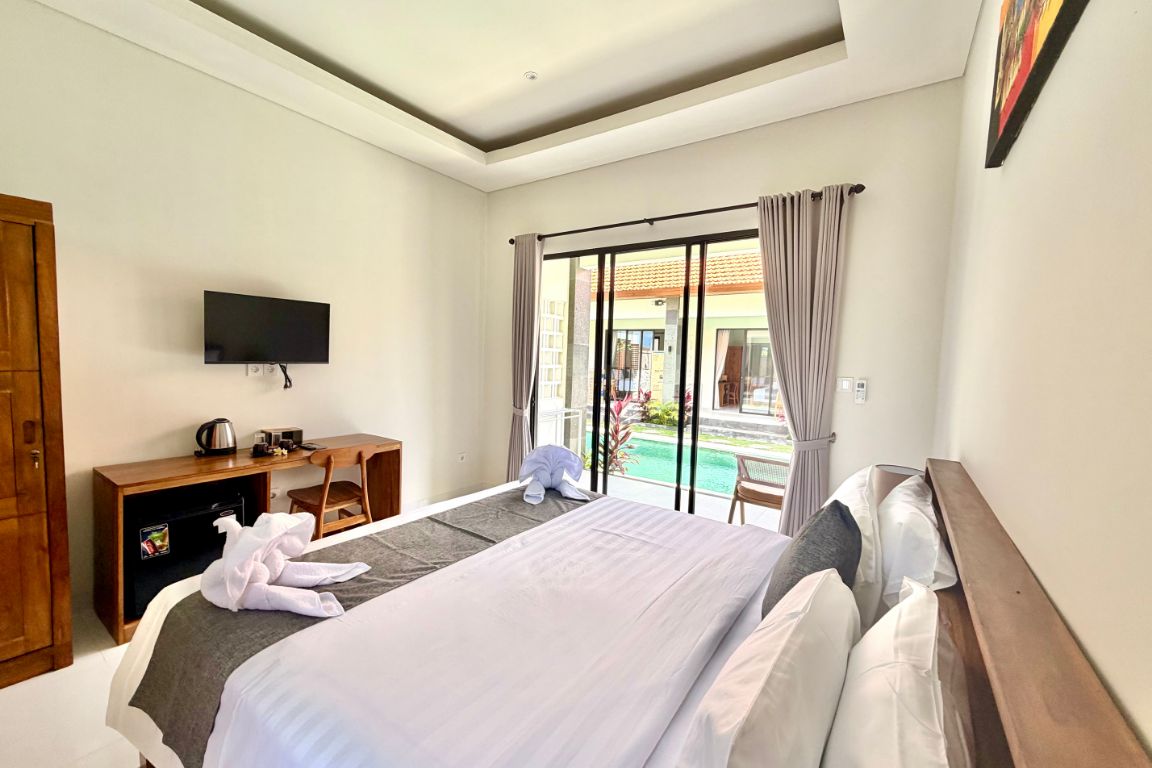 A hotel room with a bed, a desk, a television, and a view of a swimming pool.