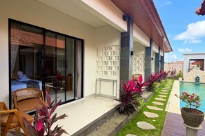 Un espacio exterior moderno con piscina, zona de estar con una silla y un sendero con plantas.