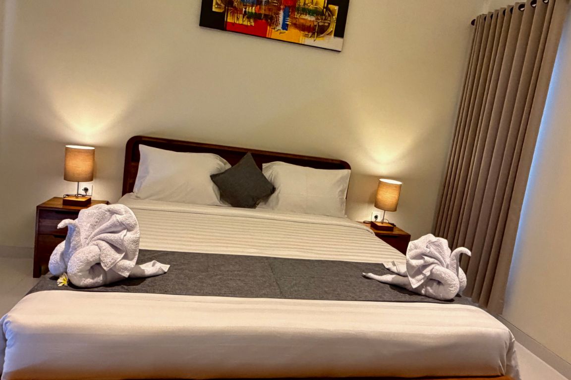 A hotel room with a bed, two bedside lamps, a painting on the wall, and a window with curtains.