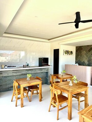 Un interior moderno con área de cocina, mesas de comedor y un ventilador de techo.