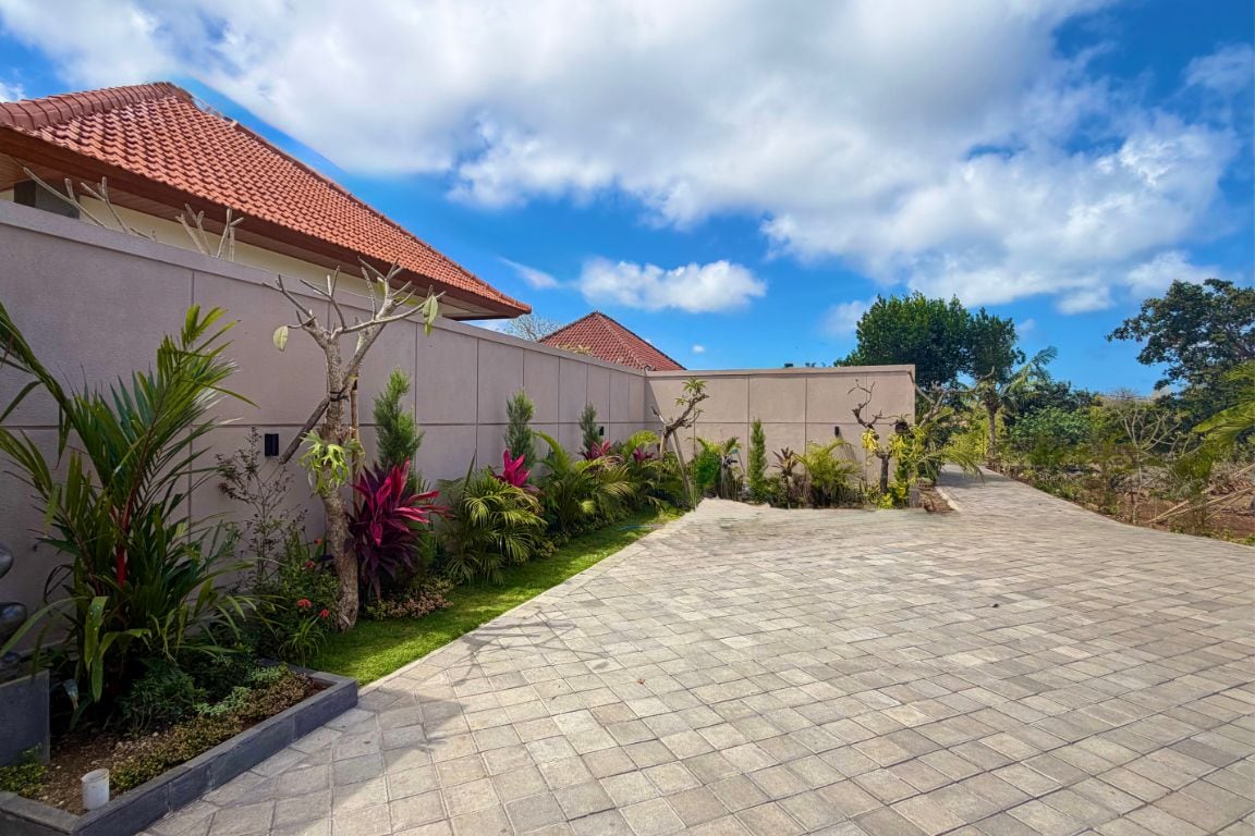 Una propiedad residencial con un camino de entrada pavimentado, un jardín con diversas plantas y un edificio con tejado de baldosas.