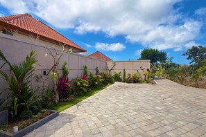 Una propiedad residencial con un camino de entrada pavimentado, un jardín con diversas plantas y un edificio con tejado de baldosas.