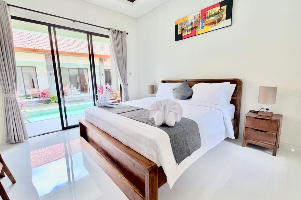 Habitación de hotel con una cama grande, una mesita de noche, una lámpara y vista a una piscina.