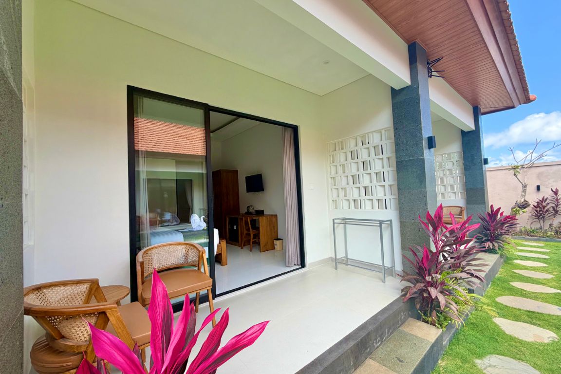 Un espacio exterior moderno con puerta de cristal que da a una habitación, una zona de estar pequeña con sillas y un jardín con piedras de adoquín.