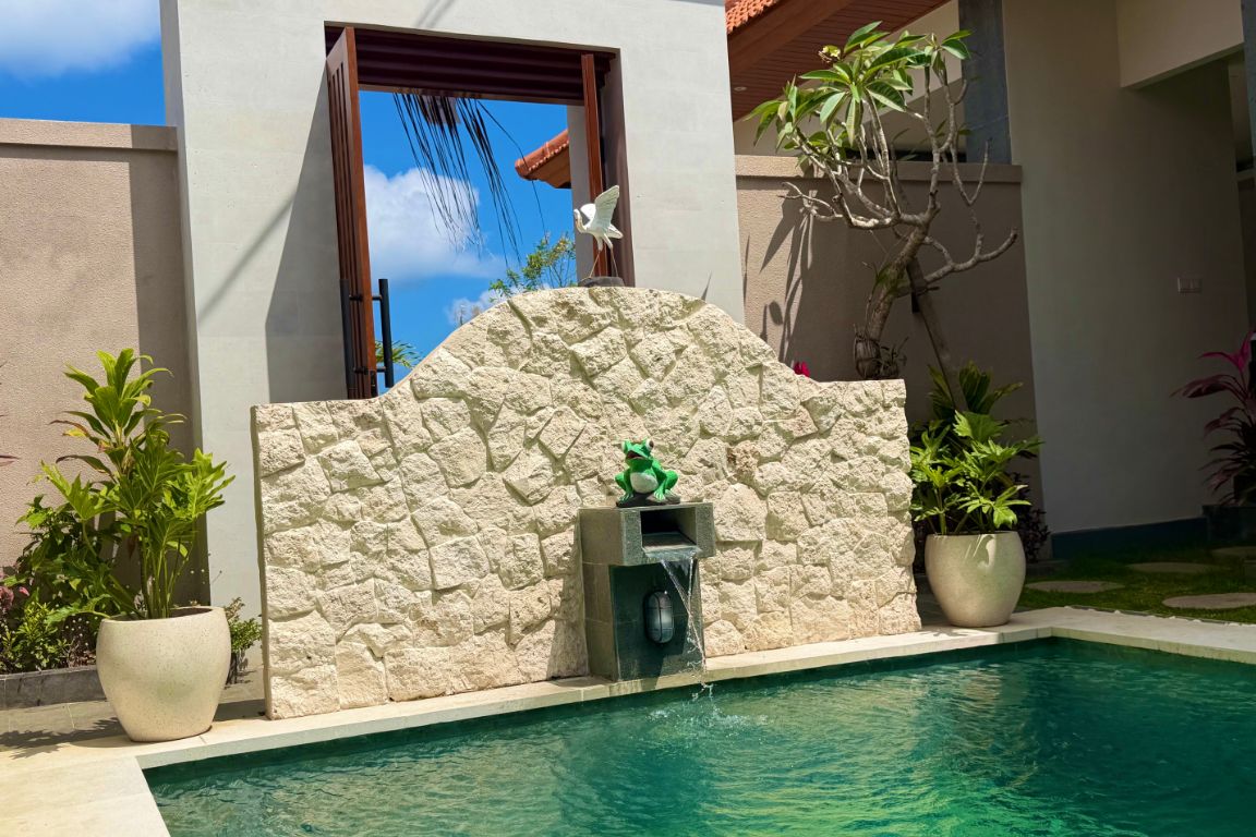 Una piscina con muro de piedra, una pequeña fuente y plantas en macetas.