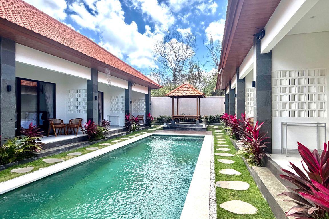 A swimming pool with a tiled roof, surrounded by a garden with stepping stones and plants.