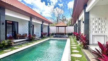 A swimming pool with a tiled roof, surrounded by a garden with stepping stones and plants.