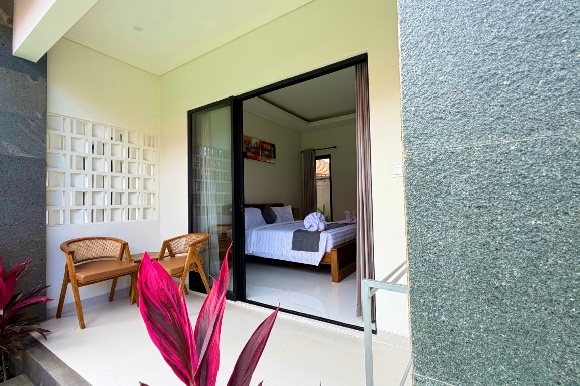 Una habitación con una cama, un espacio de descanso con sillas y una puerta de vidrio que da a otra habitación.