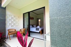 A room with a bed, a seating area with chairs, and a glass door leading to another room. - Merta Landuh Bali (Kutuh)