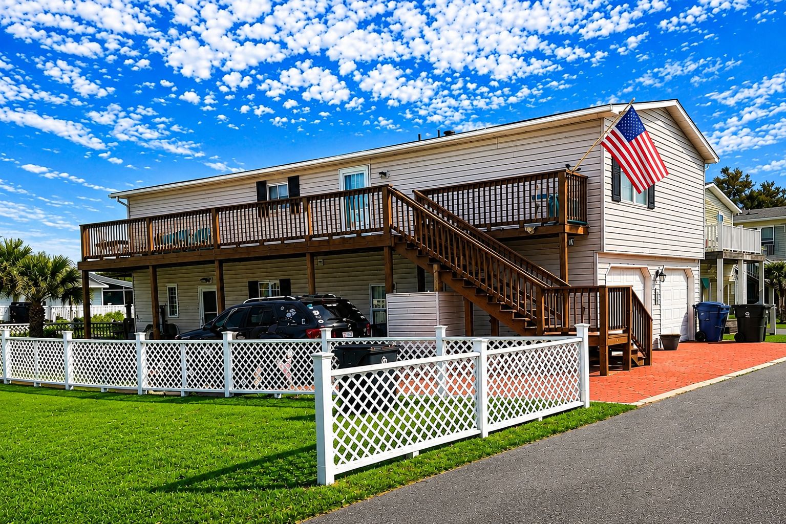 A two-story building with a balcony, an American flag, and a fenced driveway.