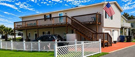 A two-story building with a balcony, an American flag, and a fenced driveway.