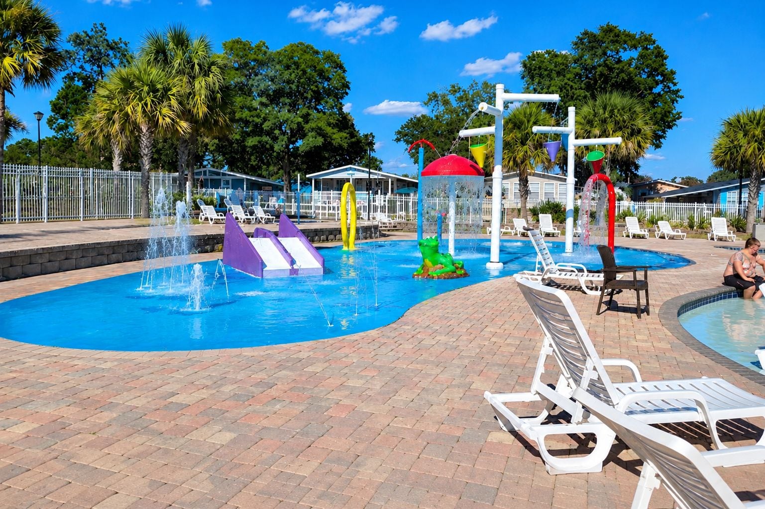 A swimming pool with water slides and a water fountain, surrounded by lounge chairs and a brick walkway.