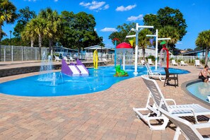 Piscina com toboáguas e fonte, rodeada por espreguiçadeiras e um caminho de tijolos.