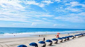 Ein Strand mit Reihen von Sonnenschirmen und Liegestühlen, ein klarer Himmel und das Meer.
