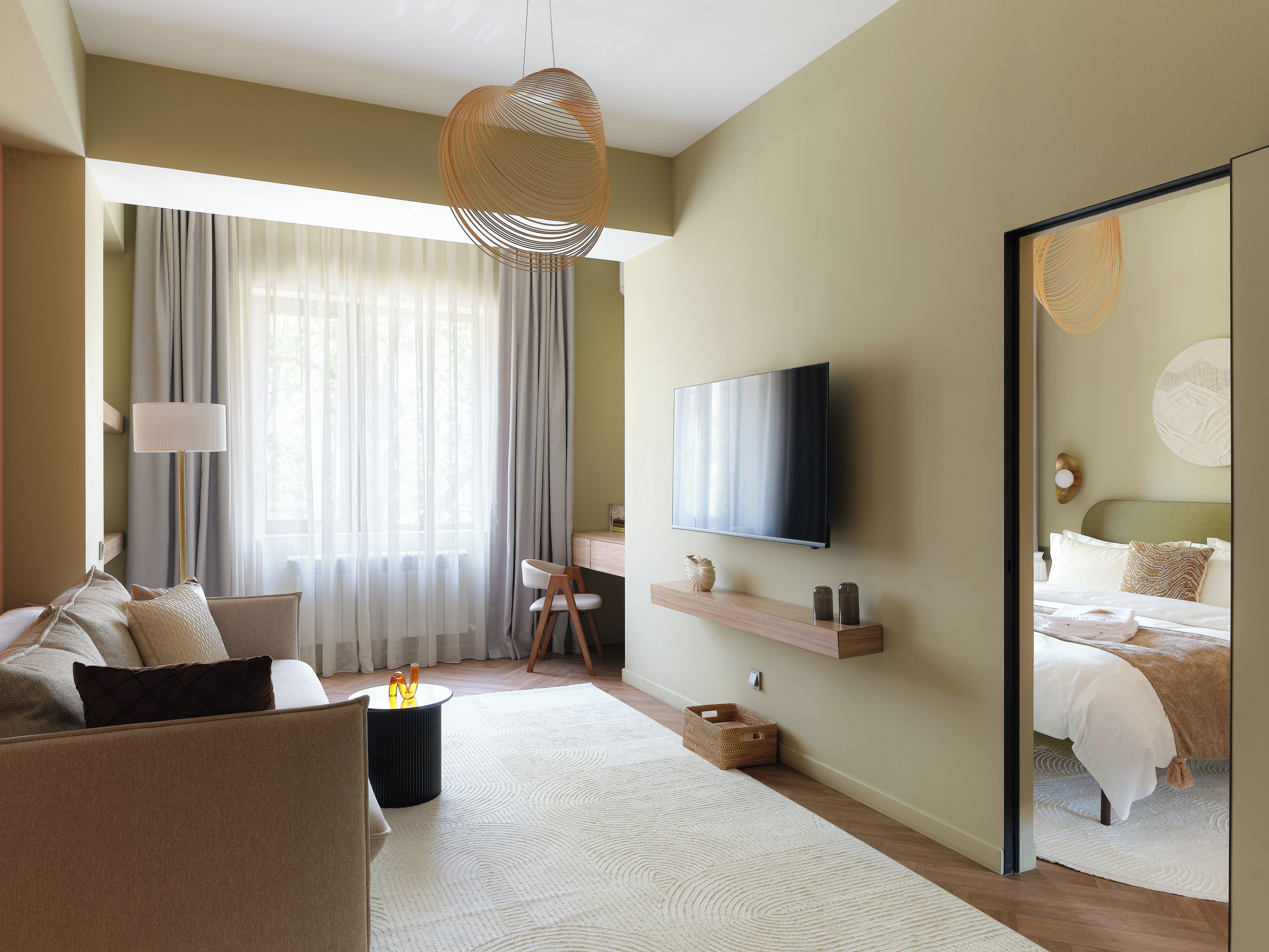 Ett modernt hotellrum med en platt-TV, en soffa, ett skrivbord och en stor spegel.