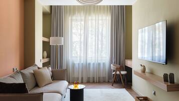 A modern living room with a sofa, a coffee table, a TV mounted on the wall, and a large window with sheer curtains.