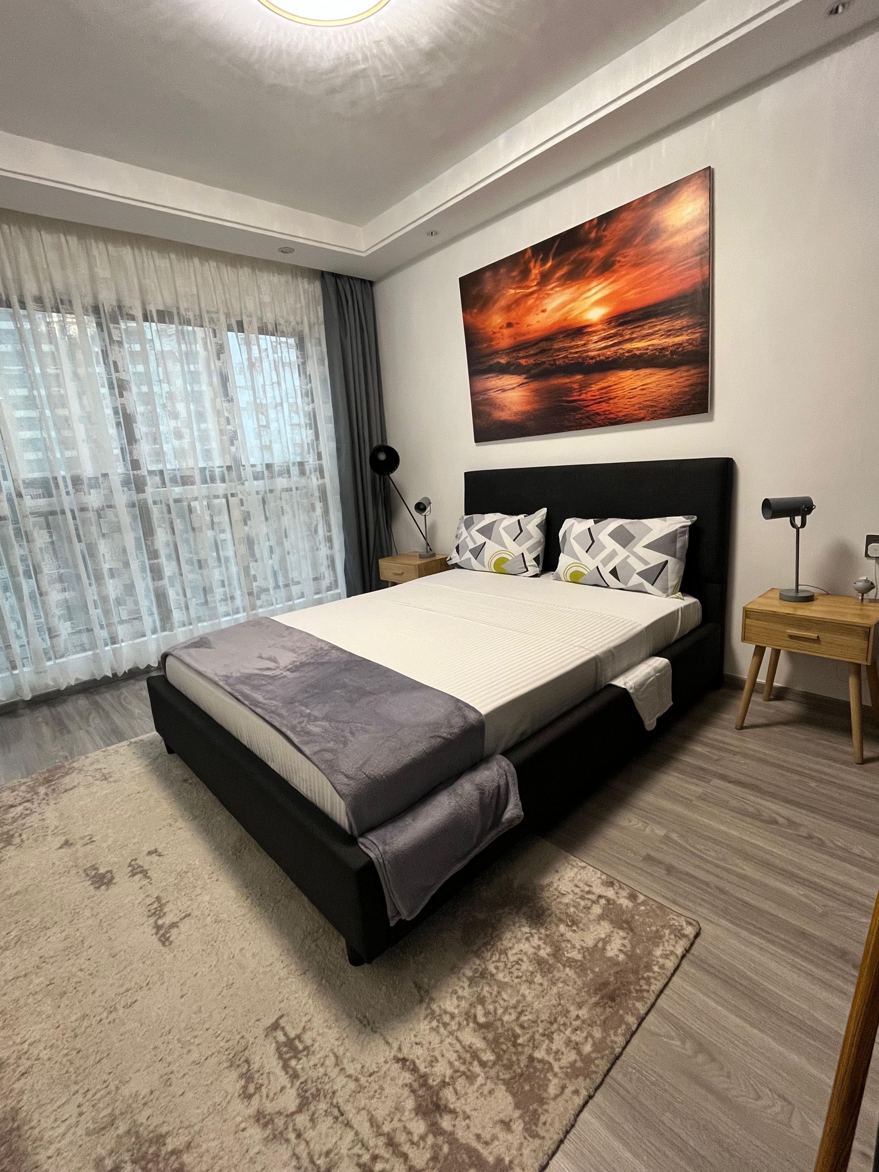 Un dormitorio moderno con una cama grande, una mesita de noche, una lámpara y un cuadro en la pared.
