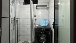 Un baño pequeño con cabina de ducha de vidrio, lavadora y lavamanos.