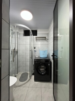 Ein kleines Badezimmer mit Duschkabine aus Glas, einer Waschmaschine und einem kleinen Waschbecken.