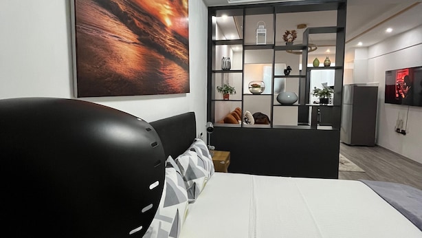Un dormitorio moderno con una cama grande, cabecera, mesita de noche y estante de pared con adornos.