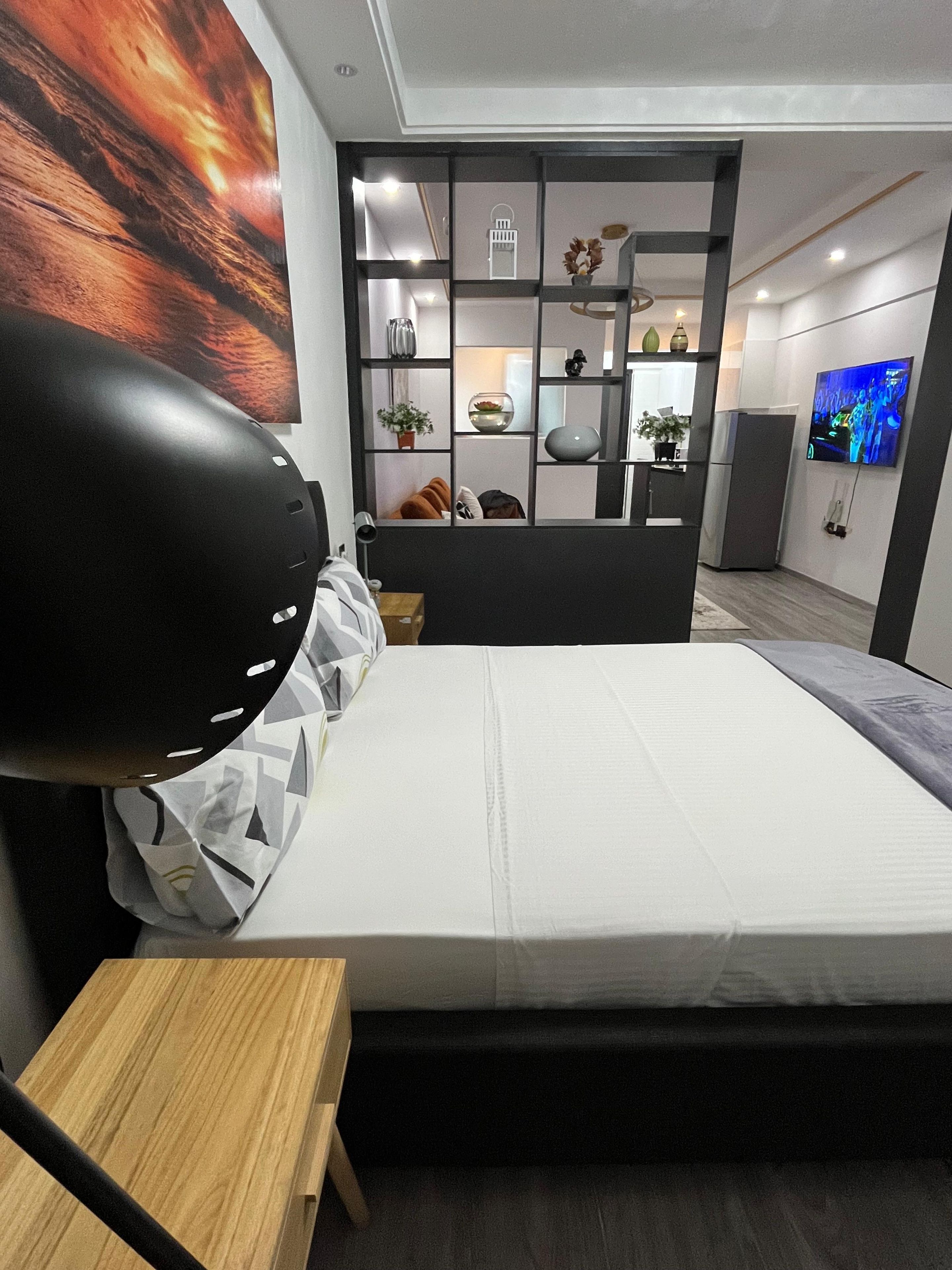 A modern bedroom with a bed, a desk, a TV, and a decorative wall unit.