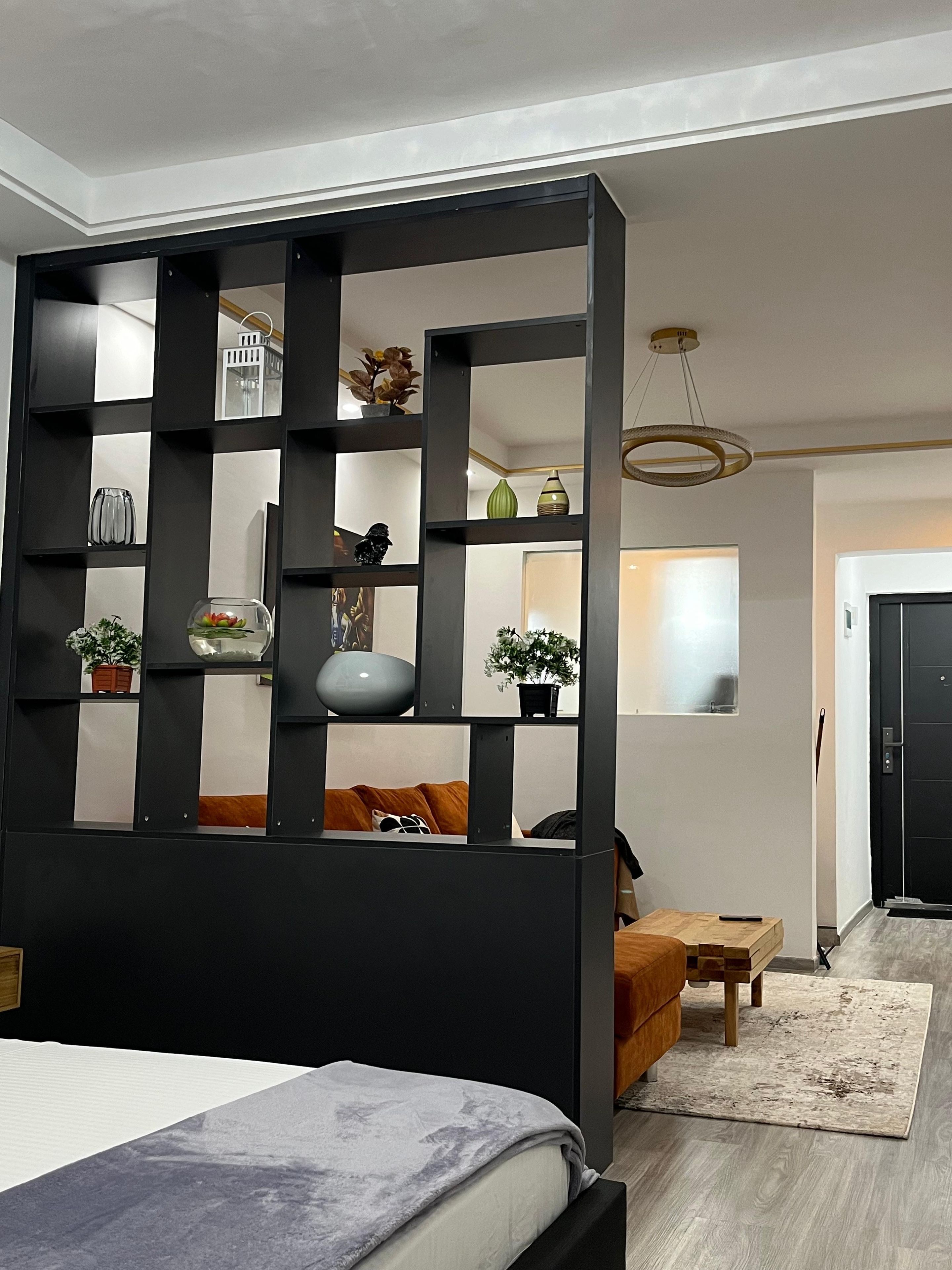 A modern bedroom with a bed, a wooden headboard, a black partition with shelves, and a small table with a chair.